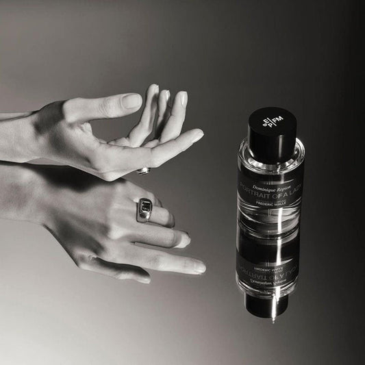 op-down view of Frederic Malle Portrait Of A Lady travel size products, featuring two spray bottles and one black canister, arranged on a reflective surface