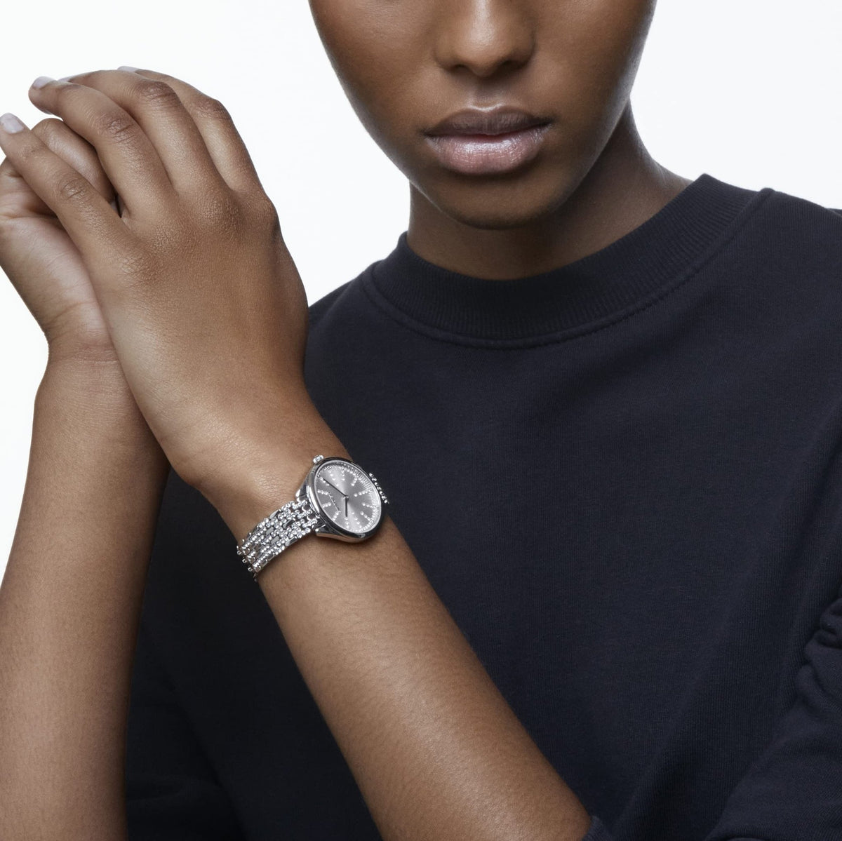 Editorial lifestyle portrait of a model wearing an exquisite crystal-embellished Swarovski luxury watch on her wrist against a clean, dark background.