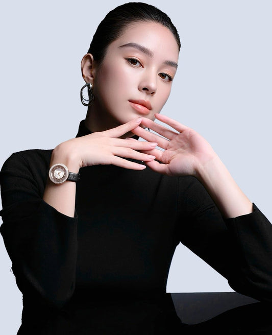 Elegant portrait of a model wearing a luxury designer wristwatch and black top against a minimalist background.