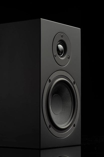 Studio product shot of a black bookshelf speaker against a dark background, highlighting its acoustic driver and tweeter.