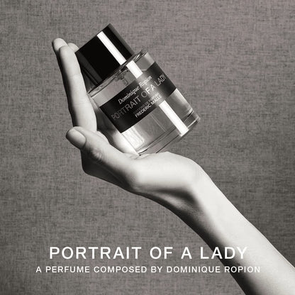 Close-up view of a Frederic Malle Portrait Of A Lady fragrance bottle held in an elegant hand against a deep background, emphasizing the label.