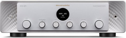 Front view of a premium silver audio receiver featuring a central display dial and multiple control knobs on a clean surface.