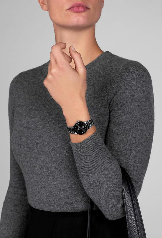 Editorial lifestyle portrait of a model wearing a sleek black ceramic Rado luxury watch against a minimalist grey background.