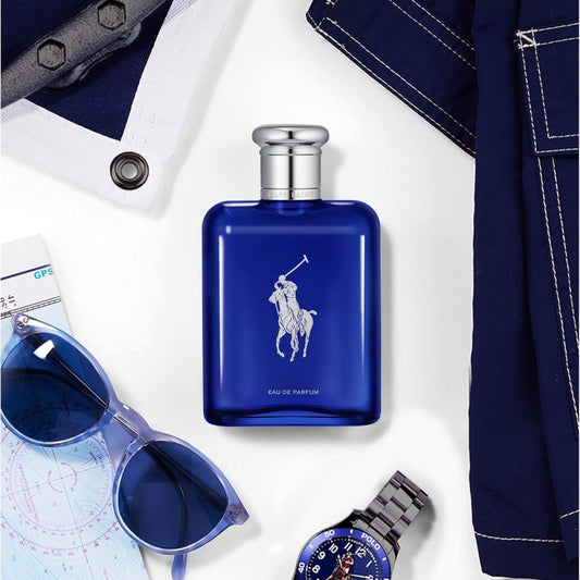 Ralph Lauren Polo Blue Eau de Parfum blue glass bottle displayed in a flat-lay arrangement with sunglasses, a wristwatch, and denim clothing against a dark background."