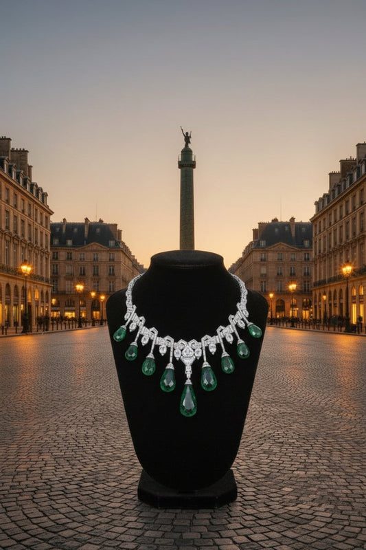 Luxurious diamond and emerald statement necklace displayed on a black bust against an atmospheric European street and monument backdrop at sunset.
